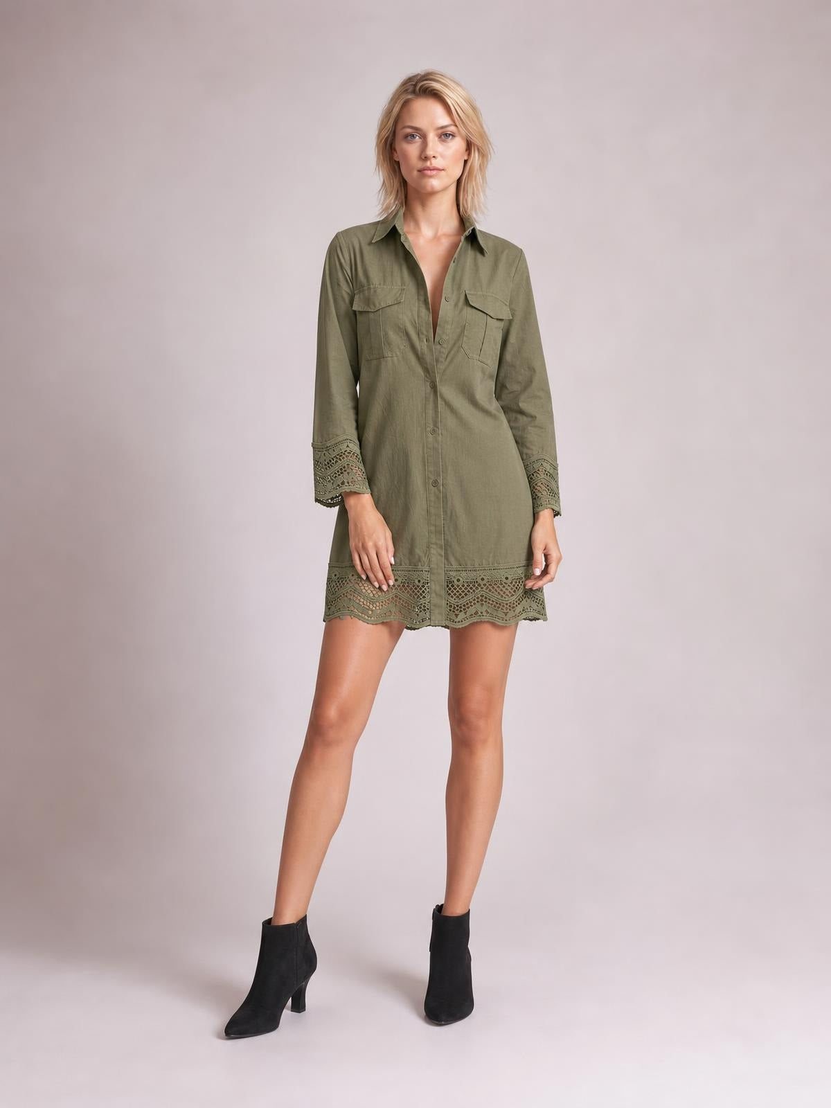 Model wears an olive green button-down shirt dress with a collared neckline, chest pockets, long sleeves, eyelet lace trim, and a relaxed mini silhouette.