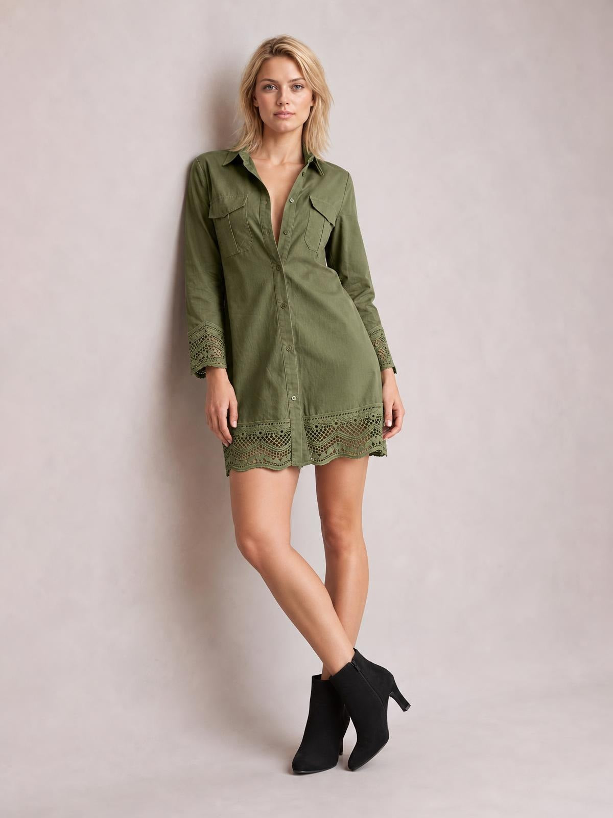 A model poses in an olive-green button-down shirt dress with a collared neckline, long sleeves, chest pockets, and lace eyelet trim at the cuffs and hem.