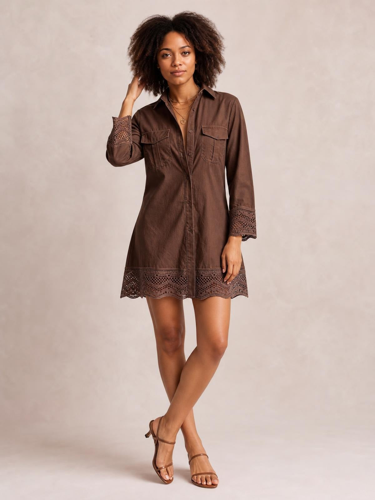 Model poses in a brown button-down shirt dress with a collared neckline, chest pockets, long lace-trimmed sleeves, and a lace-trimmed hem.