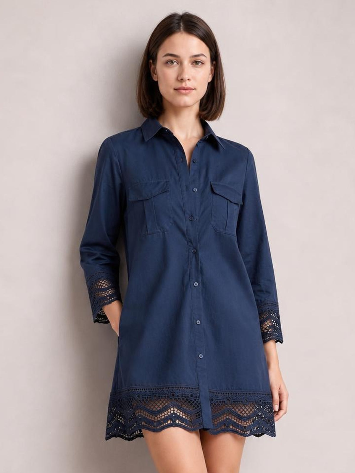 A model stands in a navy button-down shirt dress with a collared neckline, chest pockets, relaxed silhouette, and lace-trimmed cuffs and hem.