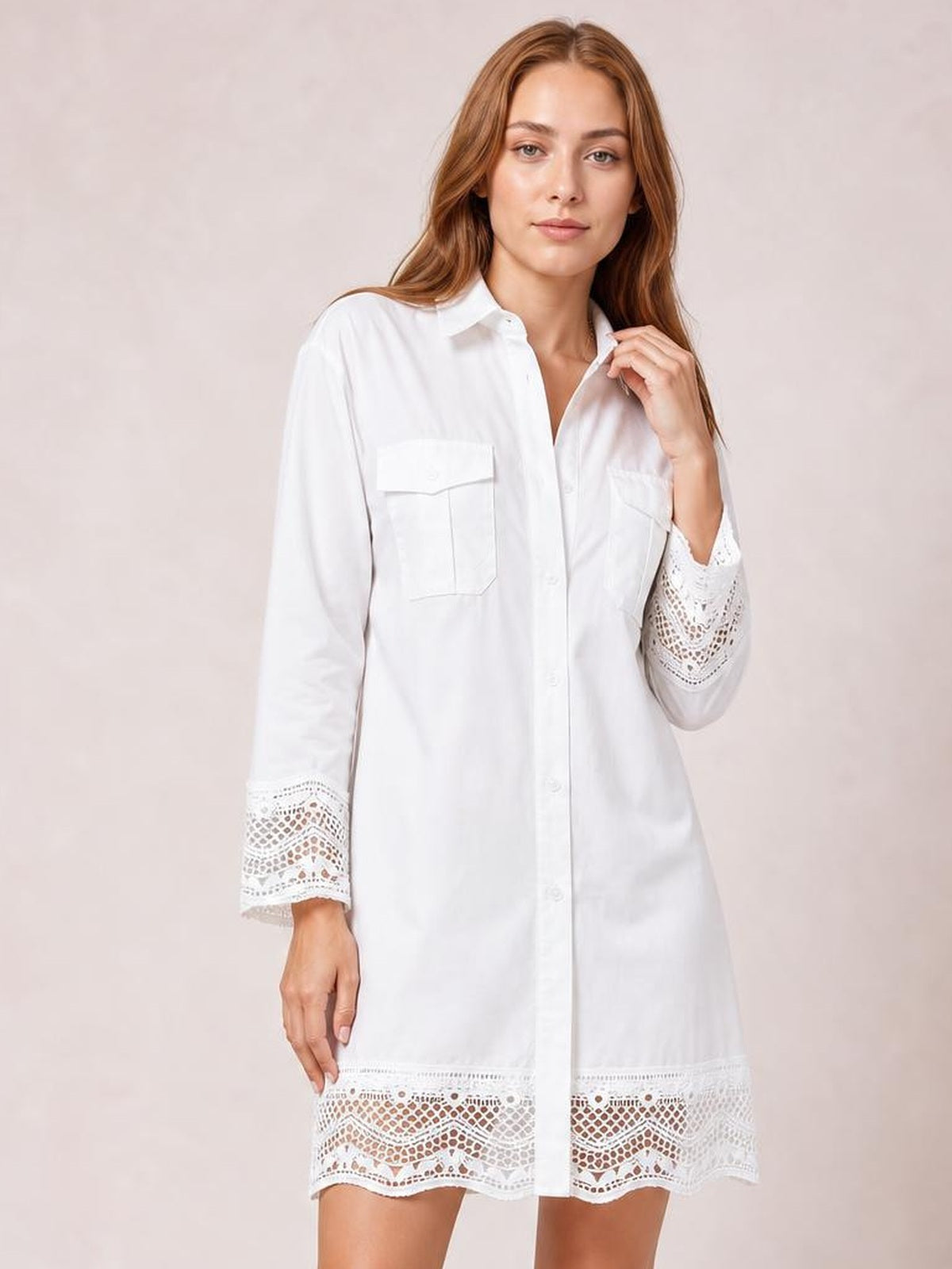 Model in a white button-down shirt dress with a relaxed silhouette, chest pockets, long sleeves, and decorative lace trim at the cuffs and hem.