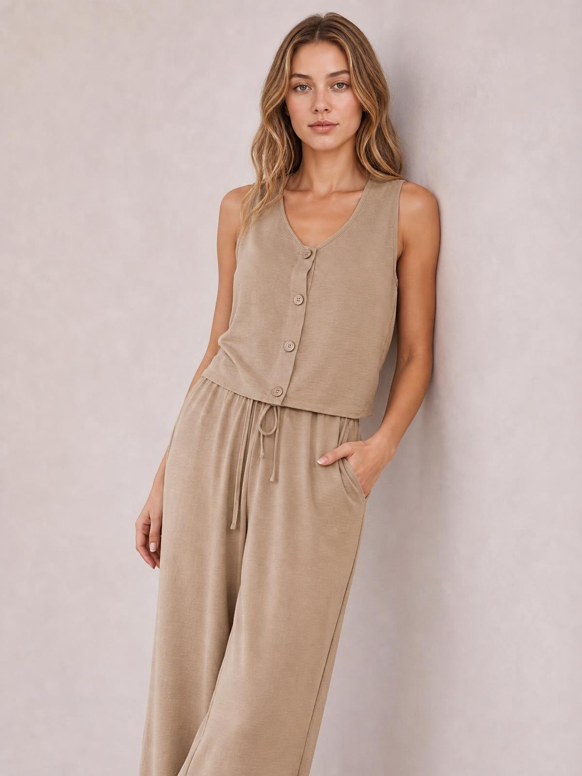A model poses with one hand in a pocket wearing a camel button-down vest and matching drawstring wide-leg pants set.