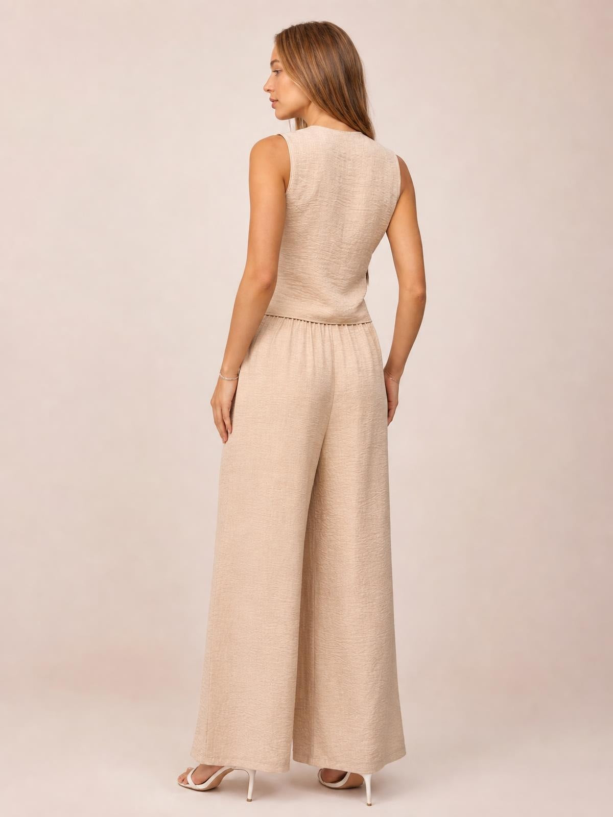 A model poses from the back in a beige button-down vest and matching high-waisted wide-leg pants set with a relaxed, flowing silhouette.