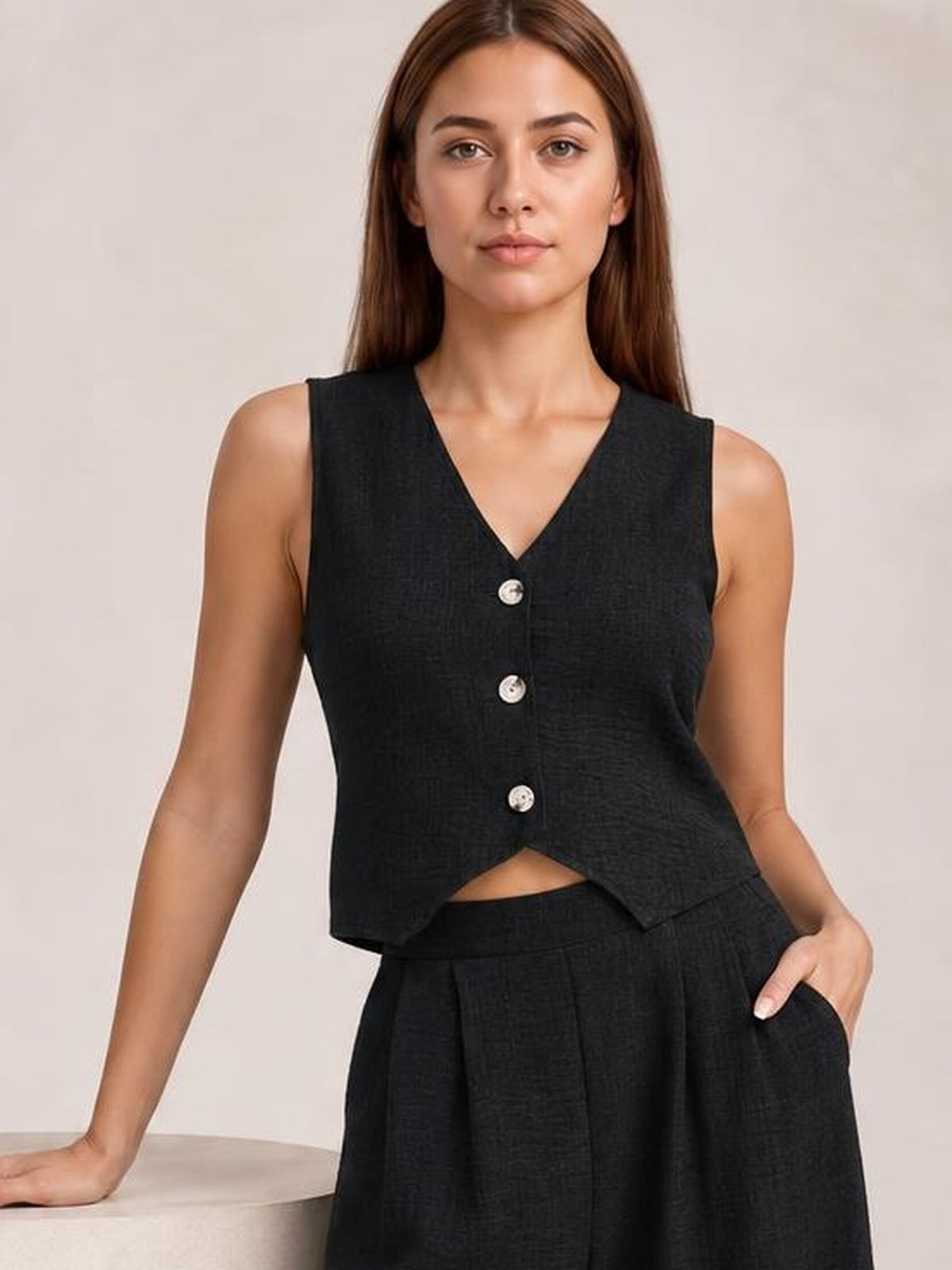 Model poses in a black button-down vest and matching wide-leg pants set, featuring a V-neck, three front buttons, relaxed silhouette, and pockets.