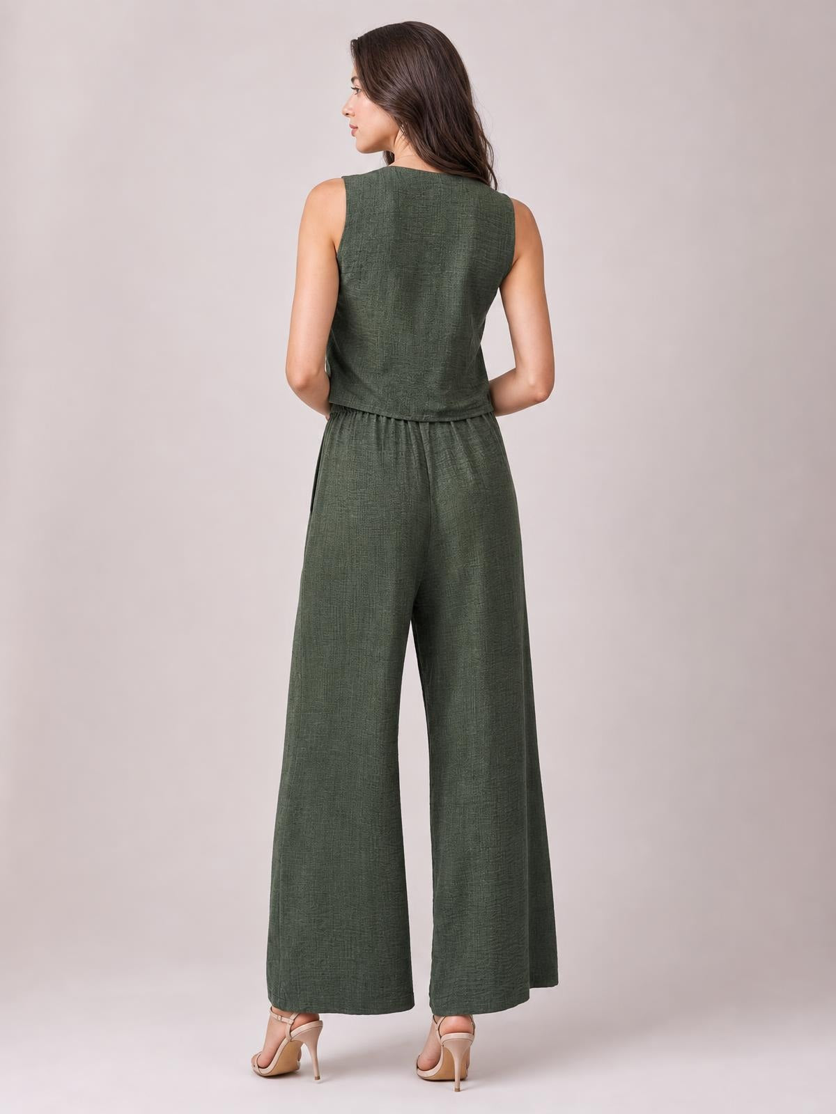 A model poses from behind in a textured olive-green sleeveless vest and matching high-waisted wide-leg pants with a fluid, relaxed silhouette.
