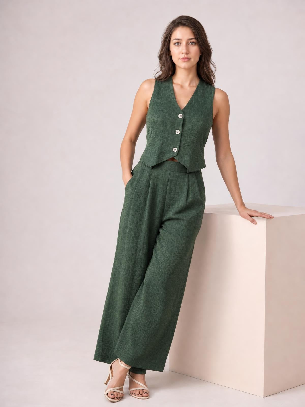 A model wears a dark green buttoned vest and matching wide-leg pants with side pockets, standing with one hand tucked in a pocket.