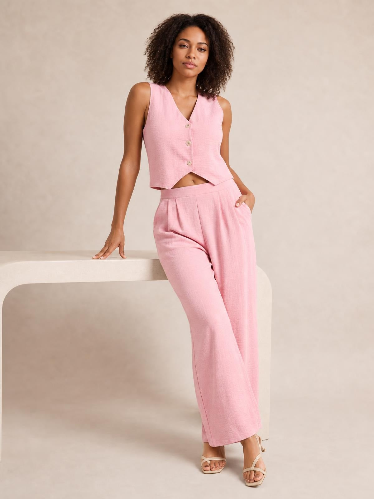 A model poses in a pink button-down vest and matching wide-leg pants set, showing the tailored sleeveless silhouette, front buttons, pleats, and side pockets.