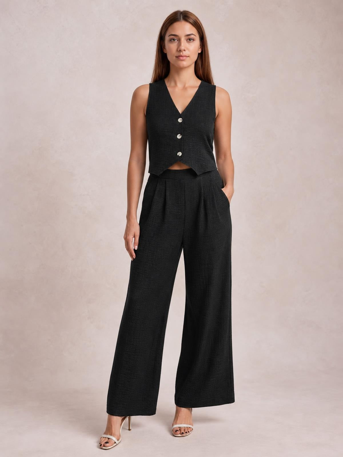 A model stands in a black button-down vest with a V-neckline and pointed hem, paired with pleated wide-leg pants featuring practical pockets.
