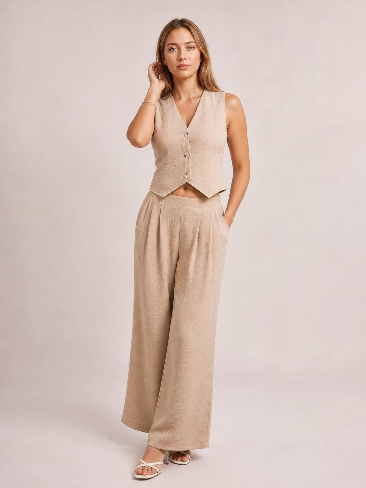 Model poses in a beige button-down vest with a V-neck and pointed hem, paired with matching high-waisted wide-leg pants and side pockets.