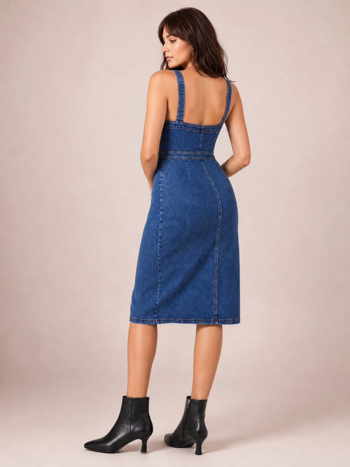 Model shown from behind in a dark blue fitted denim midi dress with wide shoulder straps, defined seaming, a shaped waist, and a straight midi hem.
