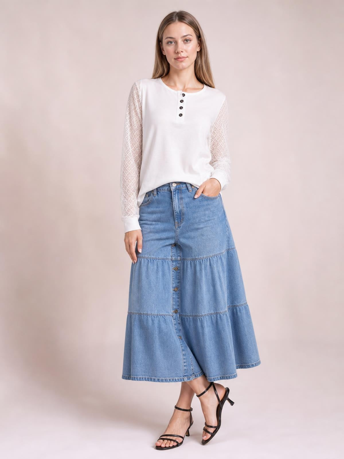 Model wears a light blue button-front tiered denim midi skirt with a relaxed A-line silhouette, paneled construction, and side pockets.