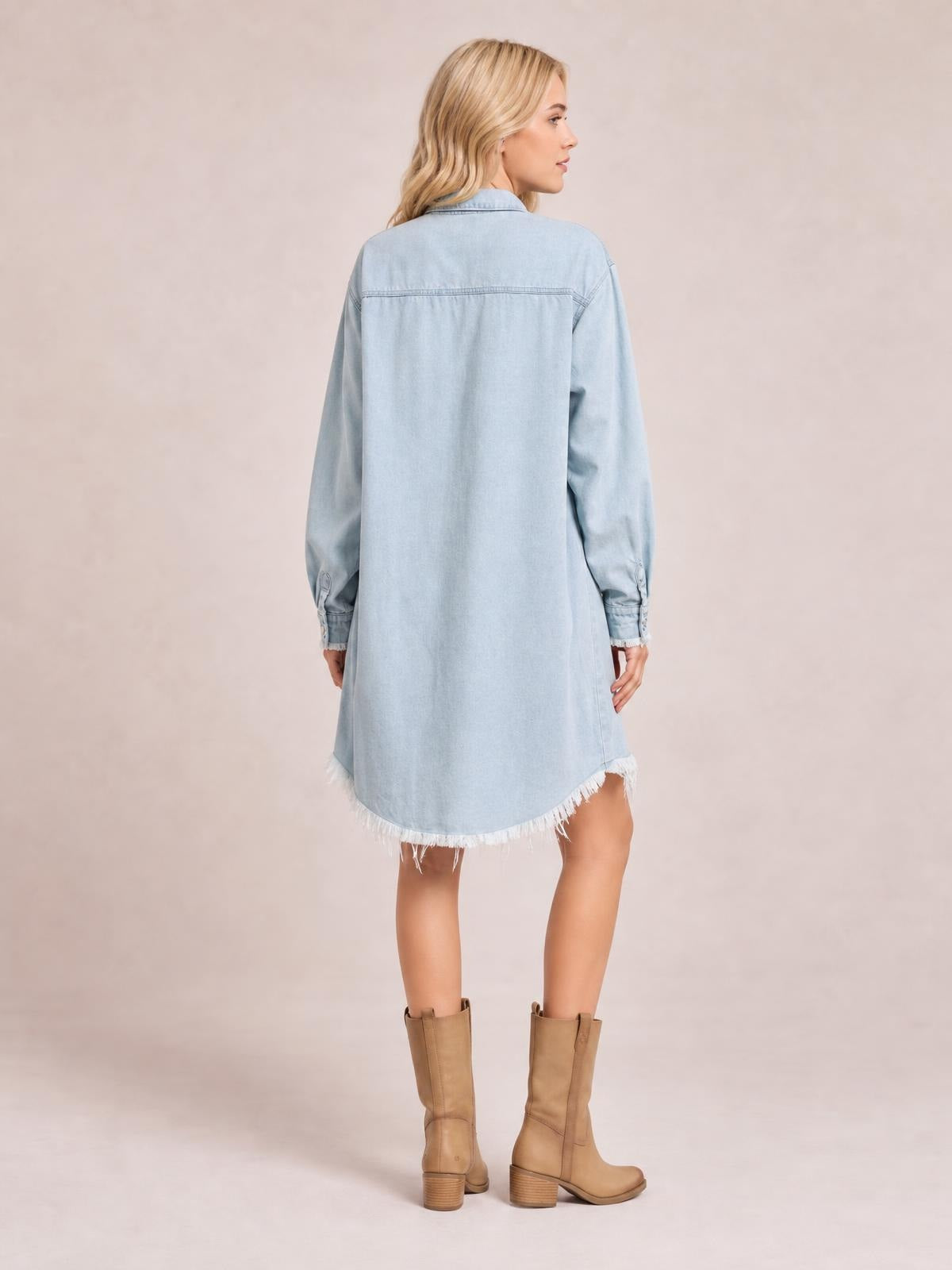 Model stands in a back view wearing a light blue denim dress with a collared neckline, long sleeves, relaxed straight silhouette, and frayed raw hem.