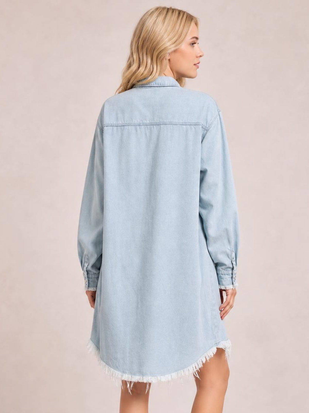 Model shown from the back in a light blue button-up collared neck denim dress with long sleeves, relaxed silhouette, seam detail, and raw hem.