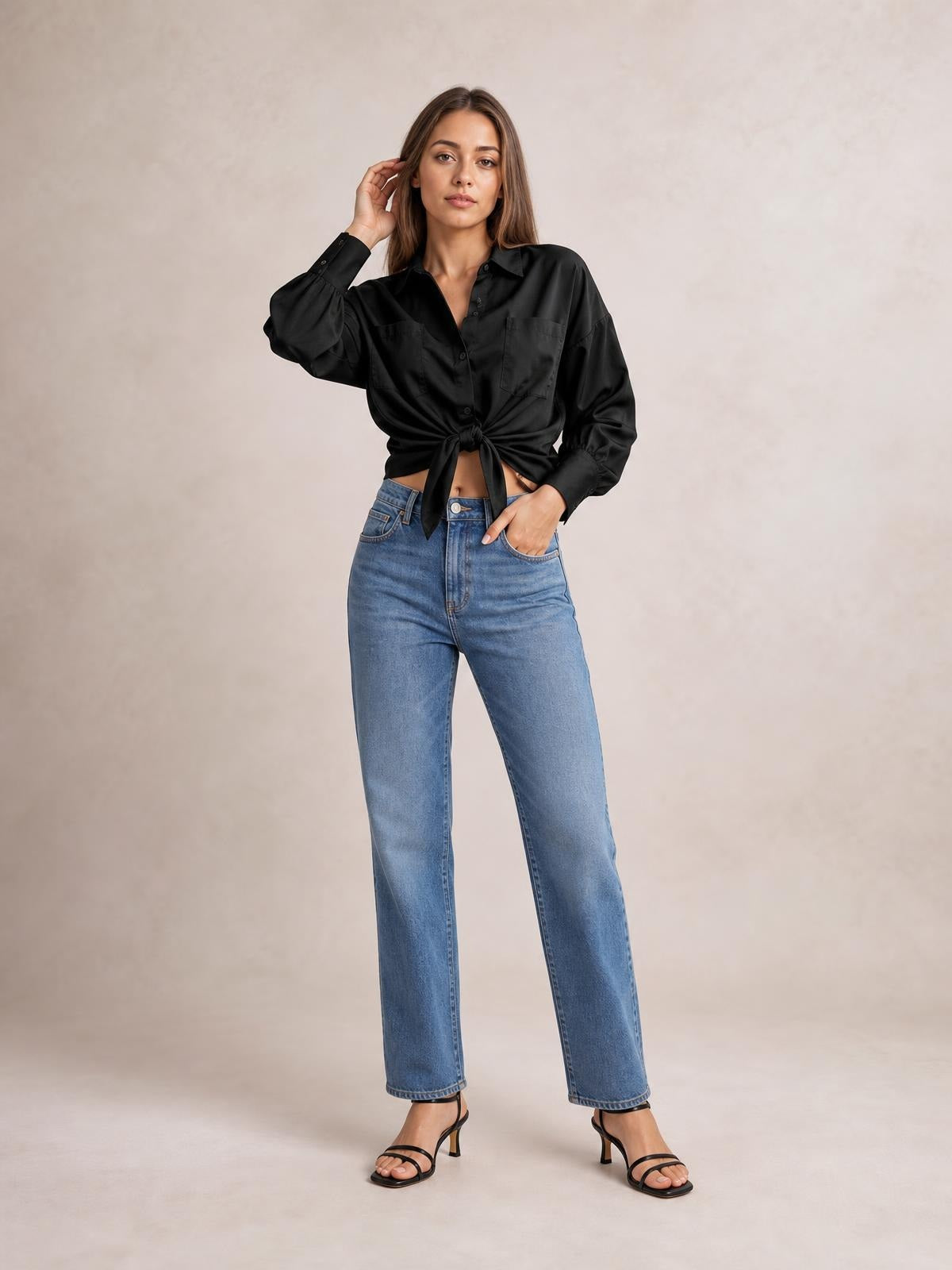 Model wearing a black button-up shirt with dropped shoulders, lantern sleeves, chest pockets, and a tied waist, posing with one hand in her jeans pocket.