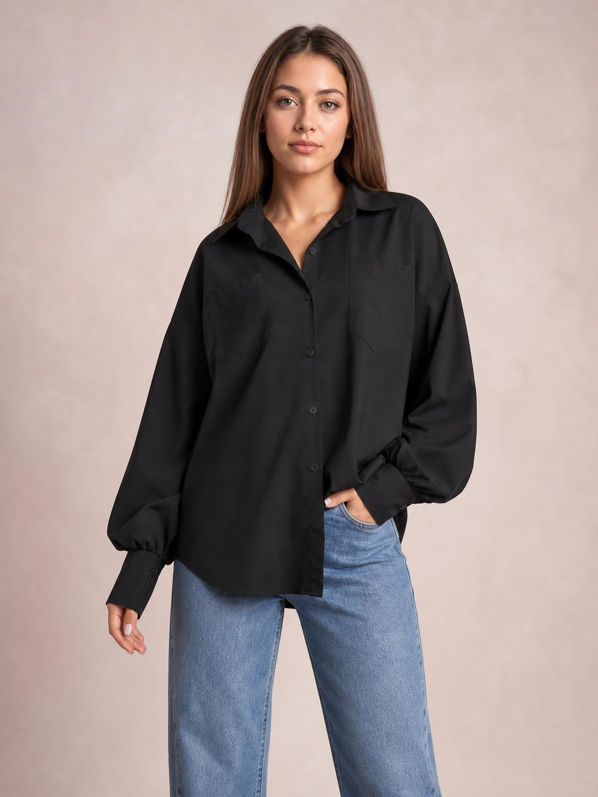 Model wears a black button-up shirt with dropped shoulders, roomy lantern sleeves, a relaxed silhouette, and two front patch pockets.