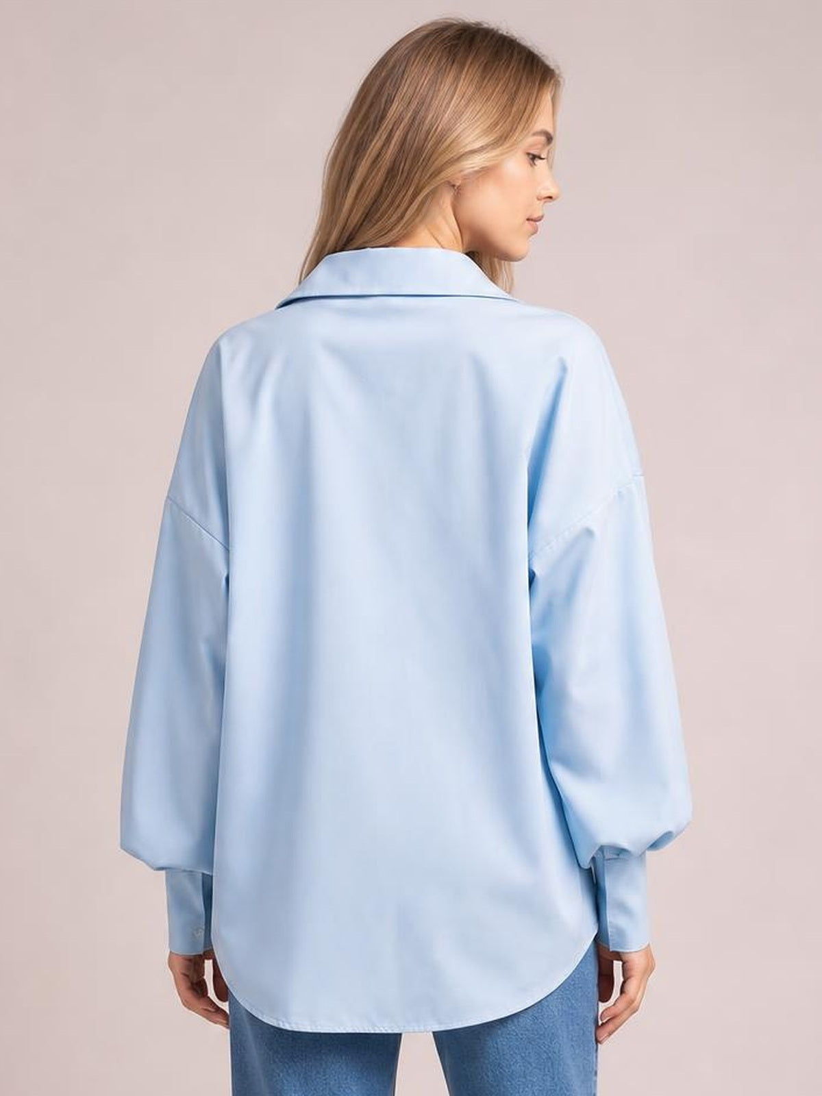 A model stands in a light blue button-up shirt shown from the back, featuring a relaxed dropped-shoulder silhouette, collared neckline, and voluminous lantern sleeves.