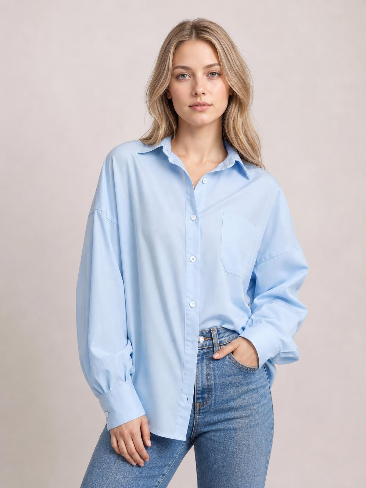 Model poses in a light blue button-up shirt with dropped shoulders, voluminous lantern sleeves, a pointed collar, and a practical chest pocket.