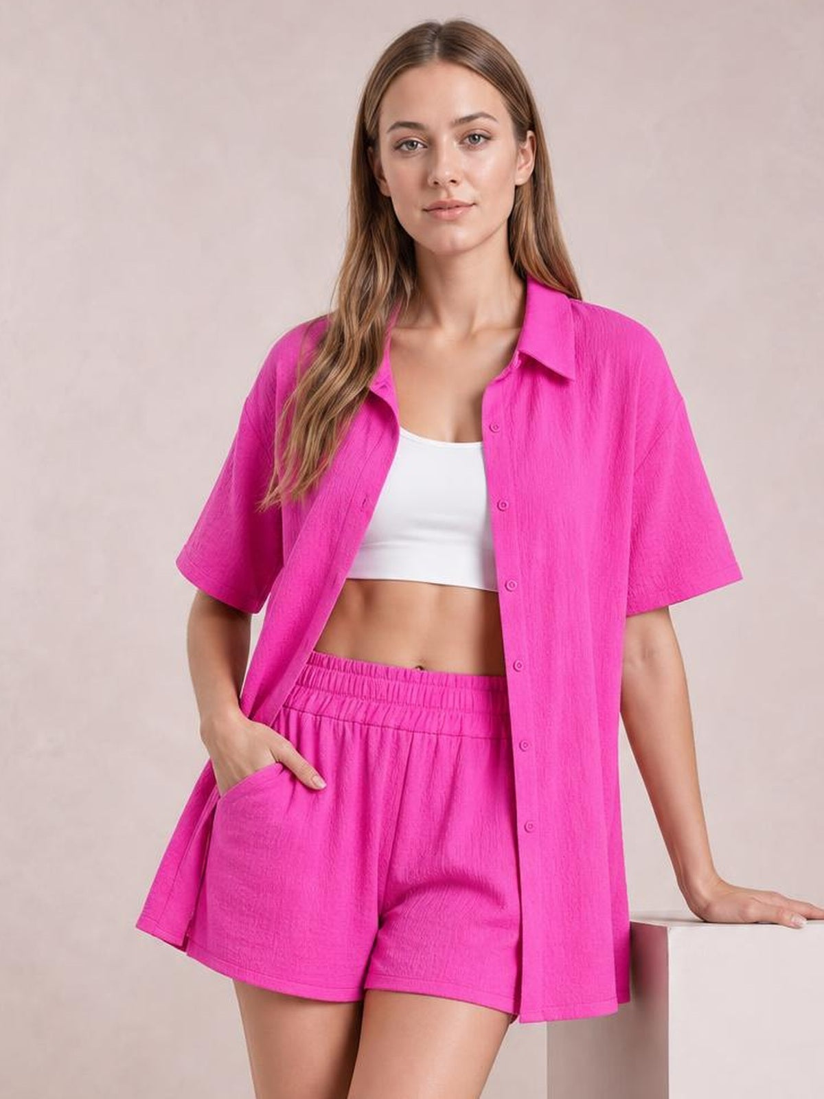 Model poses in a bright pink button-up half-sleeve top and matching pocketed shorts with an elastic waistband, worn open over a white crop top.