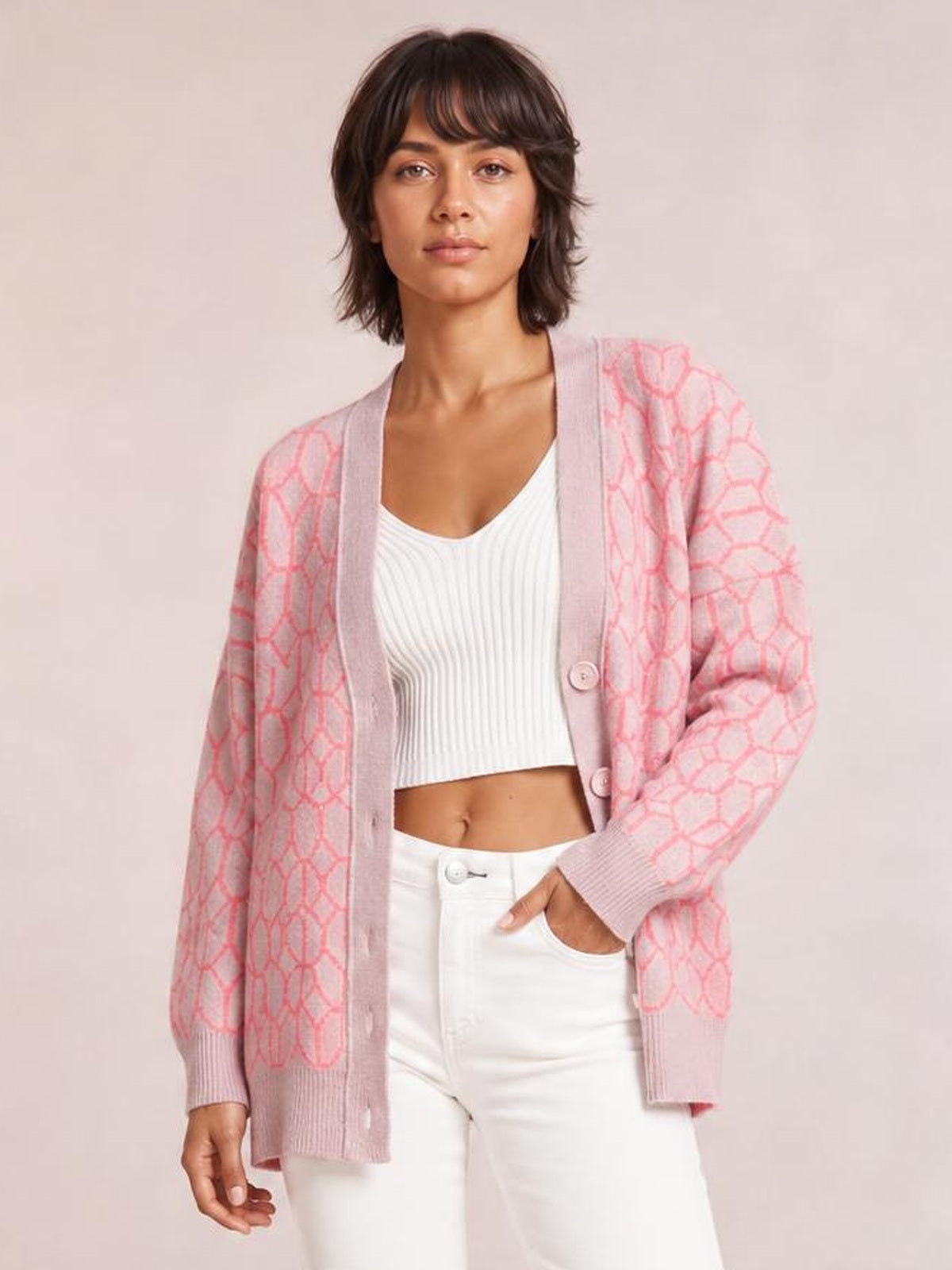 Model wears a pink patterned button-up long-sleeve cardigan with a relaxed silhouette, ribbed trim, and front buttons over a white ribbed top.