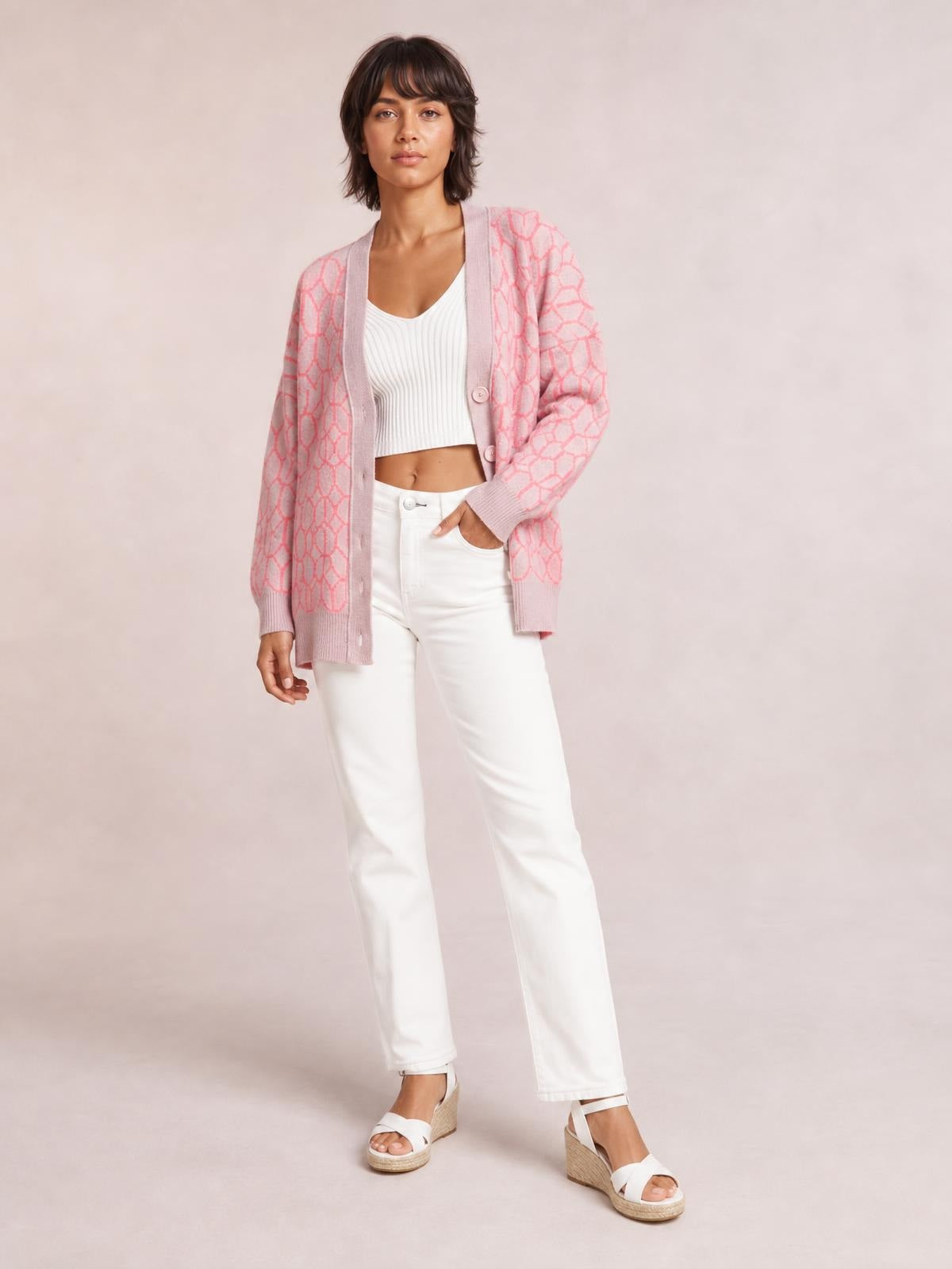 Model wears a pink patterned button-up long sleeve cardigan with a relaxed long silhouette, ribbed trim, and front buttons over a white cropped tank.