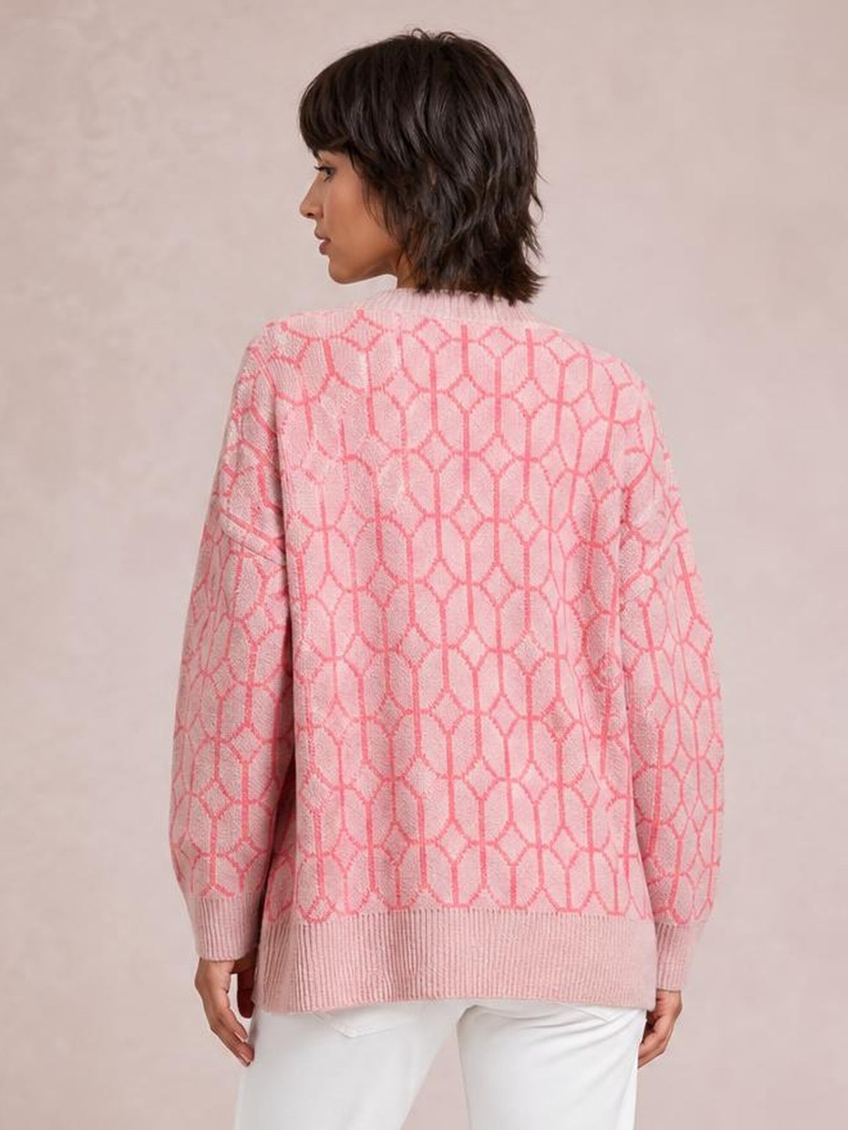 A model stands in a back view wearing a pink and white geometric-patterned long-sleeve cardigan with a relaxed silhouette and ribbed hem, cuffs, and collar.
