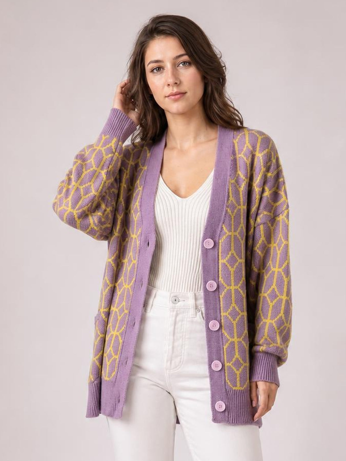 Model poses in a long-sleeve purple cardigan with yellow geometric pattern, ribbed cuffs and hem, and button-up front over a white top.