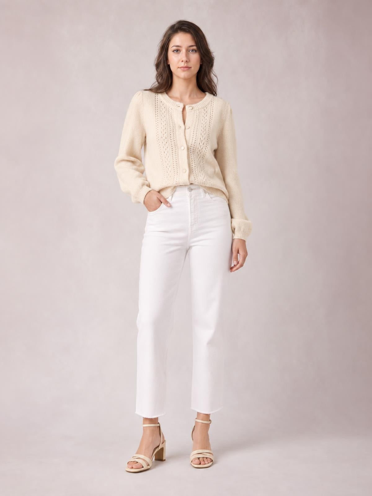 Model poses with one hand in her pocket wearing a cream button-up long sleeve cardigan with a round neck, textured knit panels, and a relaxed silhouette.