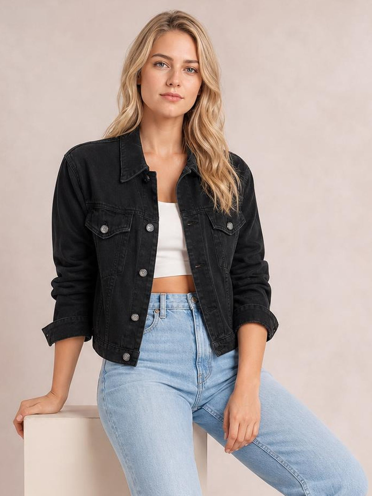 A model sits wearing a black button-up long sleeve denim jacket with a collared, structured silhouette, flap chest pockets, and rolled cuffs.