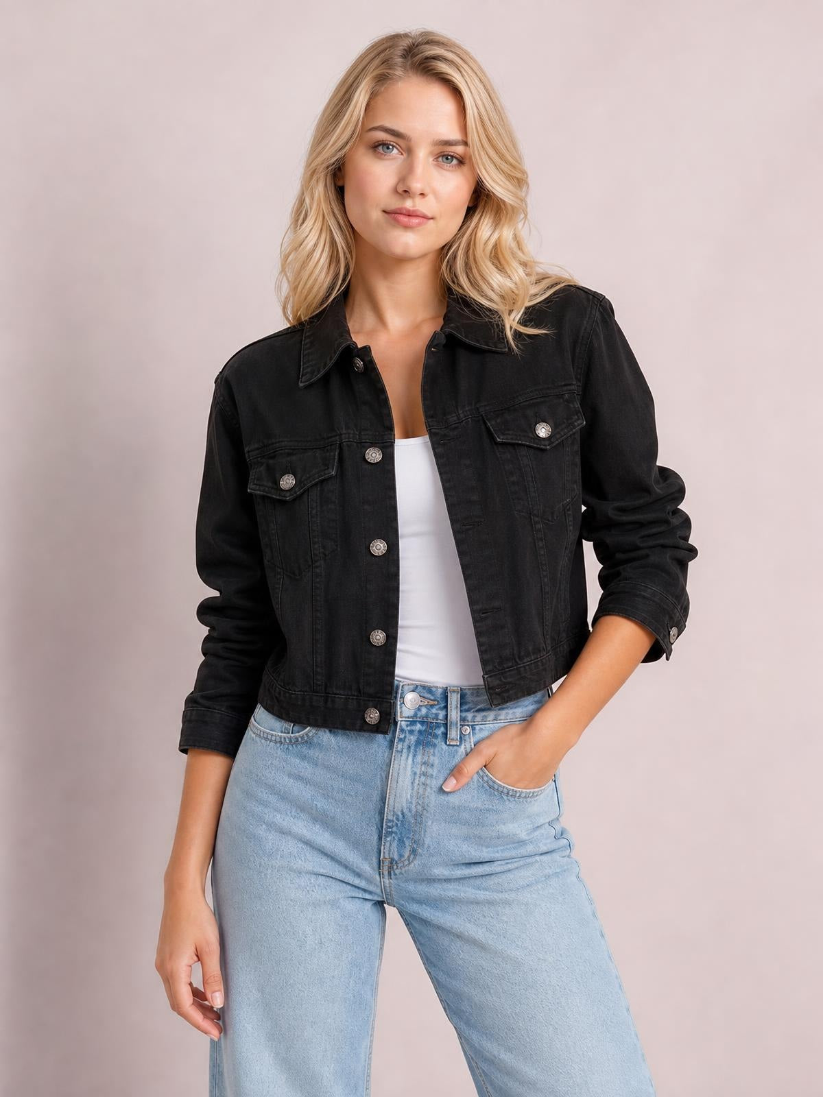Model poses in a black button-up long sleeve denim jacket with a collared cropped silhouette, chest flap pockets, and rolled cuffs.