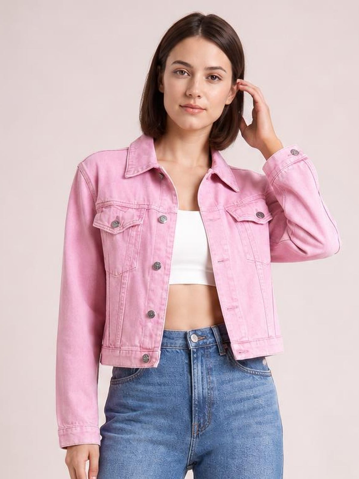 Model wearing a pink button-up long sleeve denim jacket with a collared neckline, flap chest pockets, seam detailing, and a waist-length silhouette, posing with one hand in her hair.