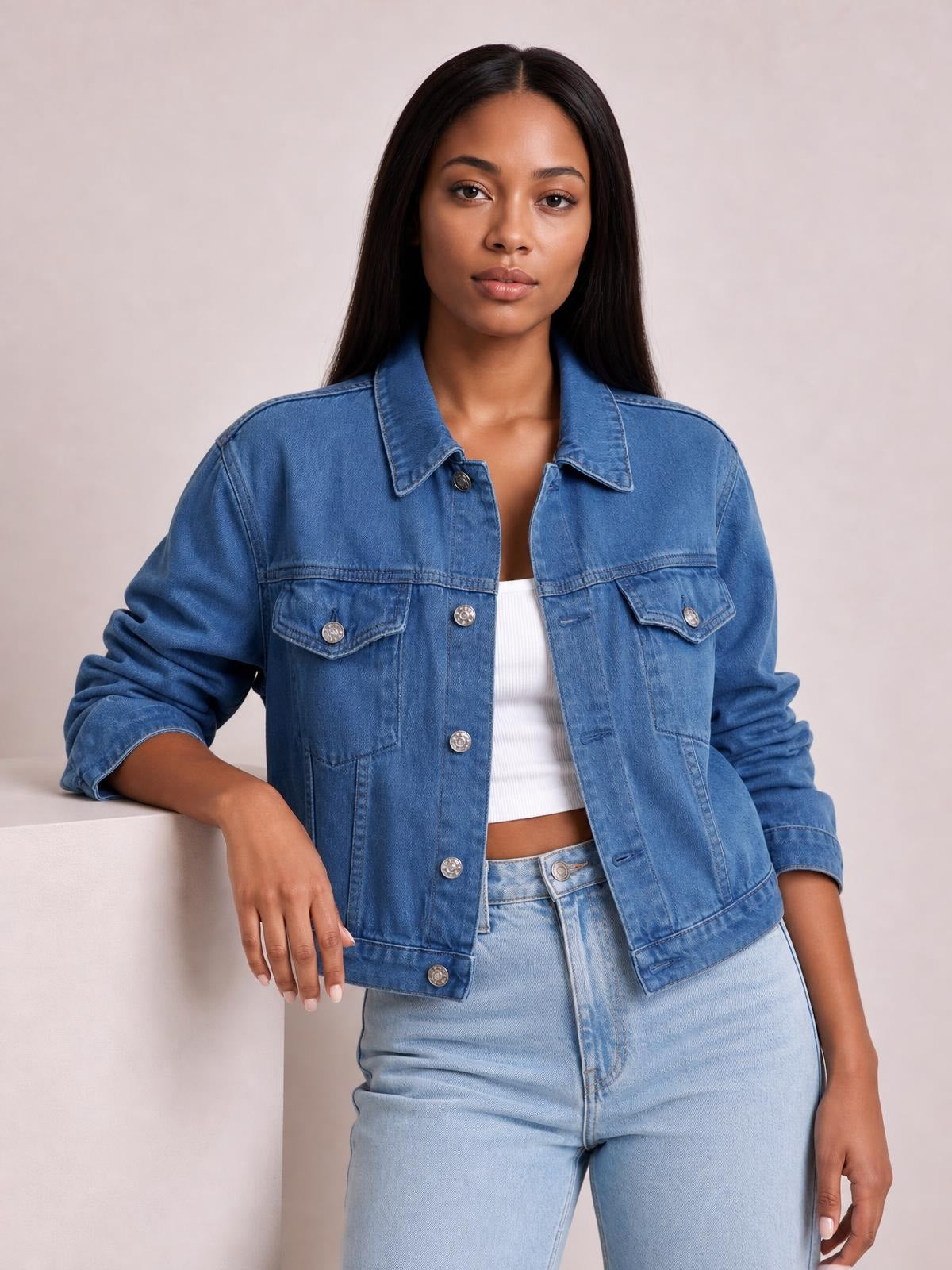 Model wears a blue button-up long sleeve denim jacket with a collared, relaxed silhouette, flap chest pockets, and rolled cuffs.