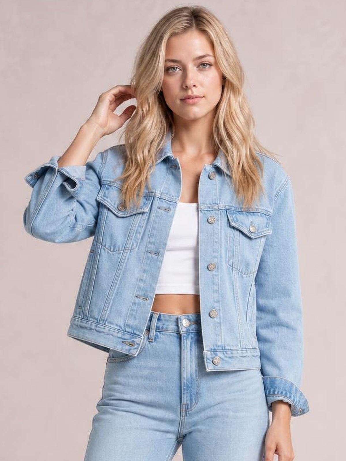 Model poses in a light blue button-up long sleeve denim jacket with a relaxed fit, flap chest pockets, metal buttons, and rolled cuffs.