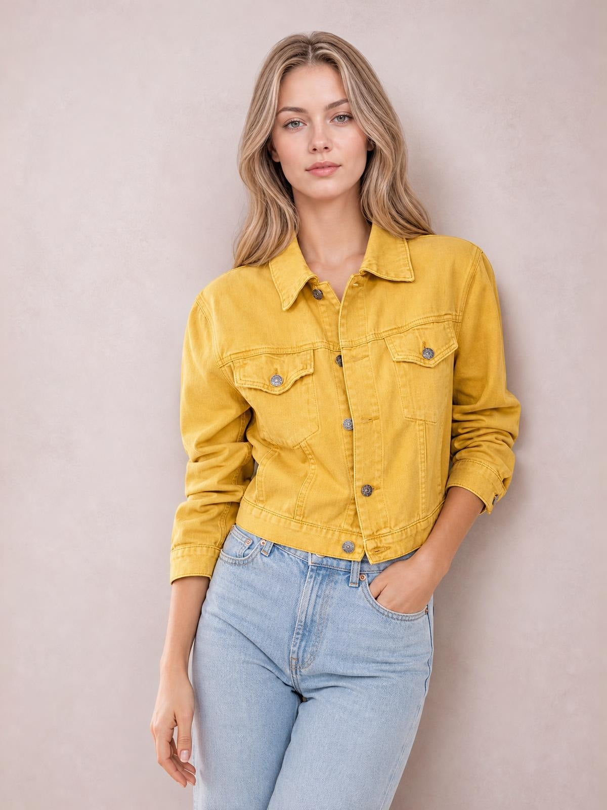 Model poses in a mustard yellow button-up long sleeve denim jacket with a collared neckline, flap chest pockets, and a fitted waist-length silhouette.