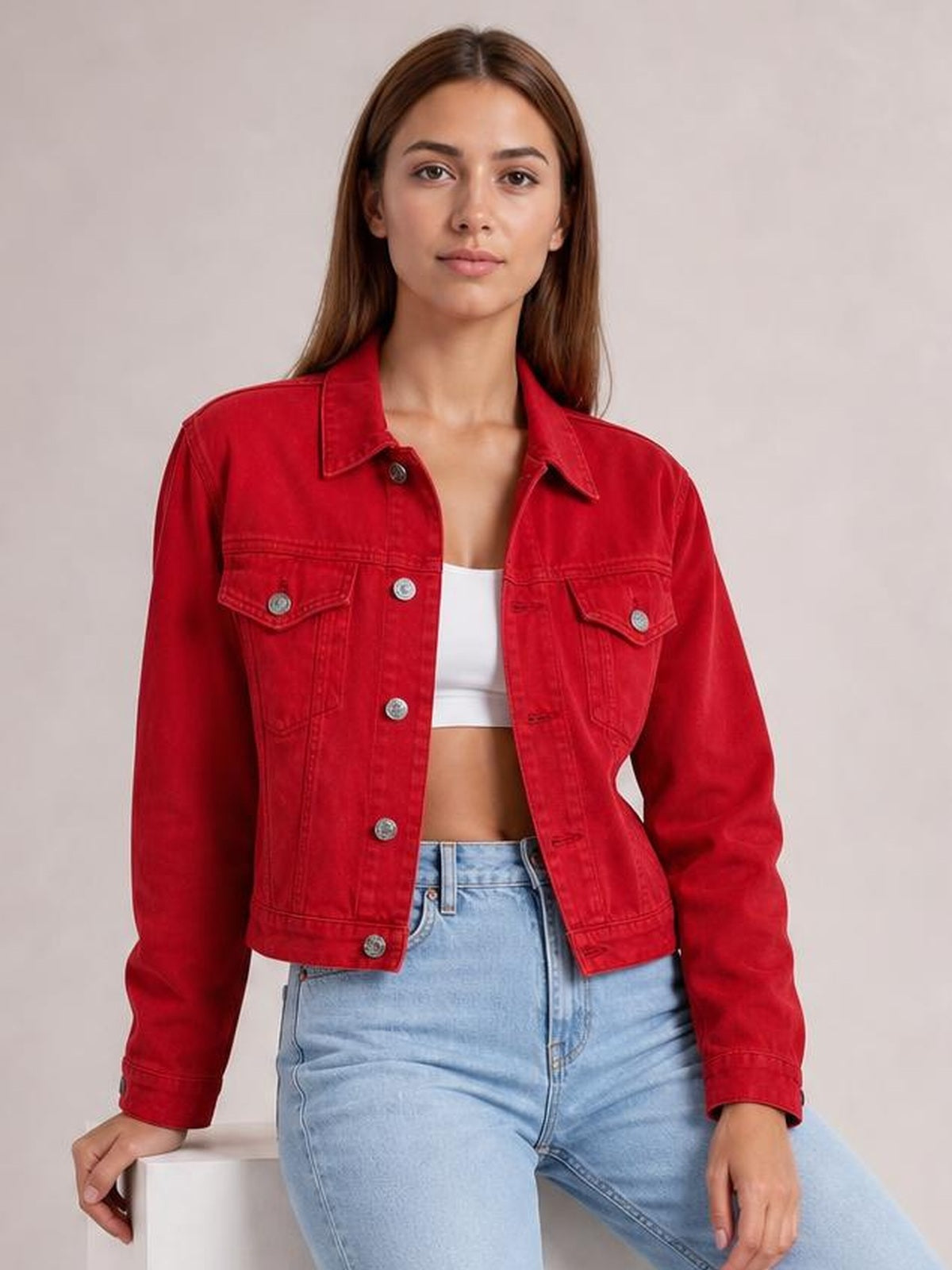 Model wears a red button-up long sleeve denim jacket with a collared neckline, flap chest pockets, and a cropped straight silhouette while seated.