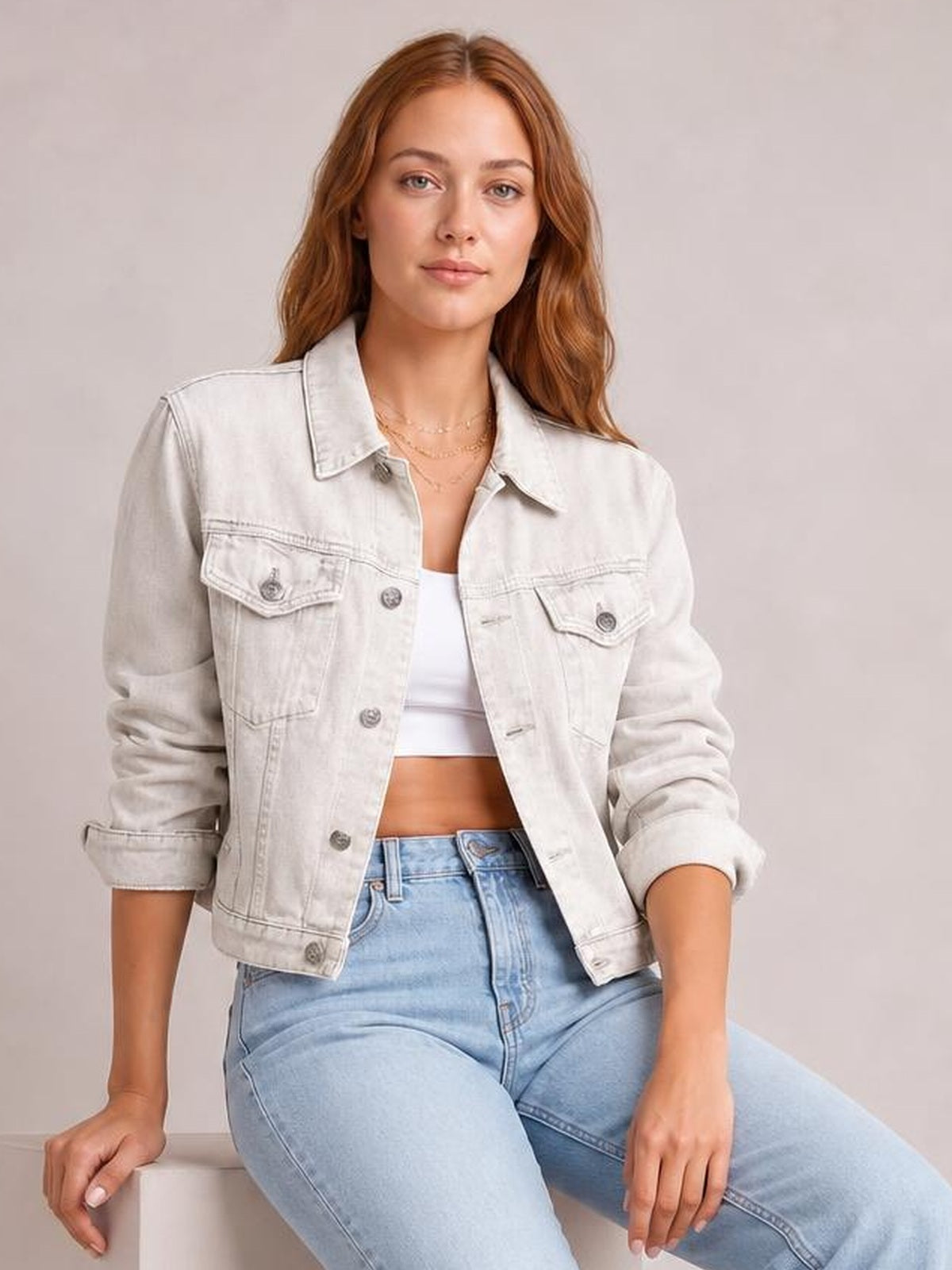 A seated model wears a light-wash denim jacket with a button front, pointed collar, long sleeves rolled at the cuffs, and flap chest pockets.