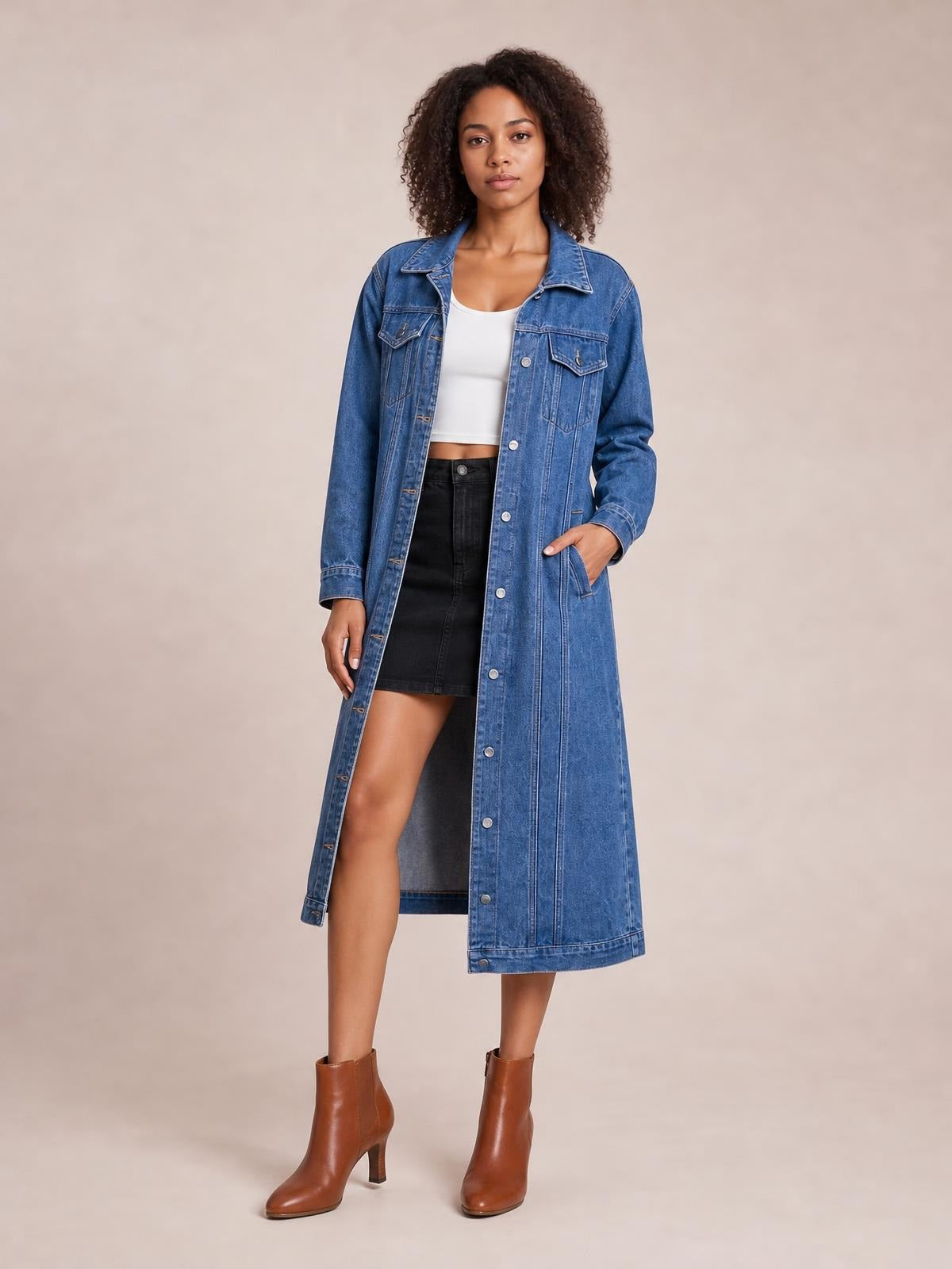 Model wearing a blue longline denim jacket with long sleeves, button front, chest and side pockets, and a straight ankle-length silhouette.
