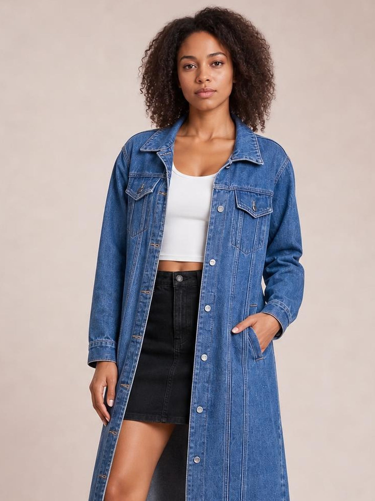 Model wears a blue longline denim jacket with long sleeves, button front, pointed collar, chest and side pockets, and a straight silhouette.