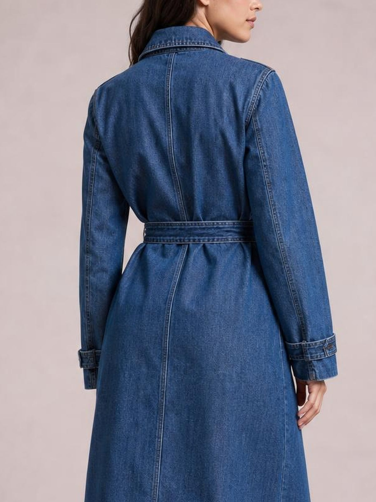 Model shown from behind wearing a blue longline denim jacket with long sleeves, a collared back, buttoned cuffs, and a defined waist belt.