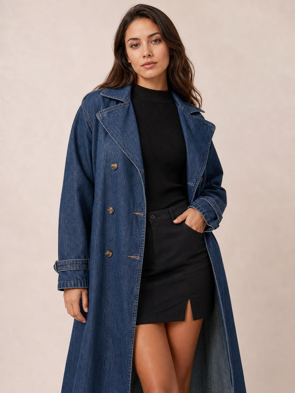 A model poses in a blue longline denim jacket with long sleeves, wide lapels, button front, cuff straps, and a relaxed straight silhouette.