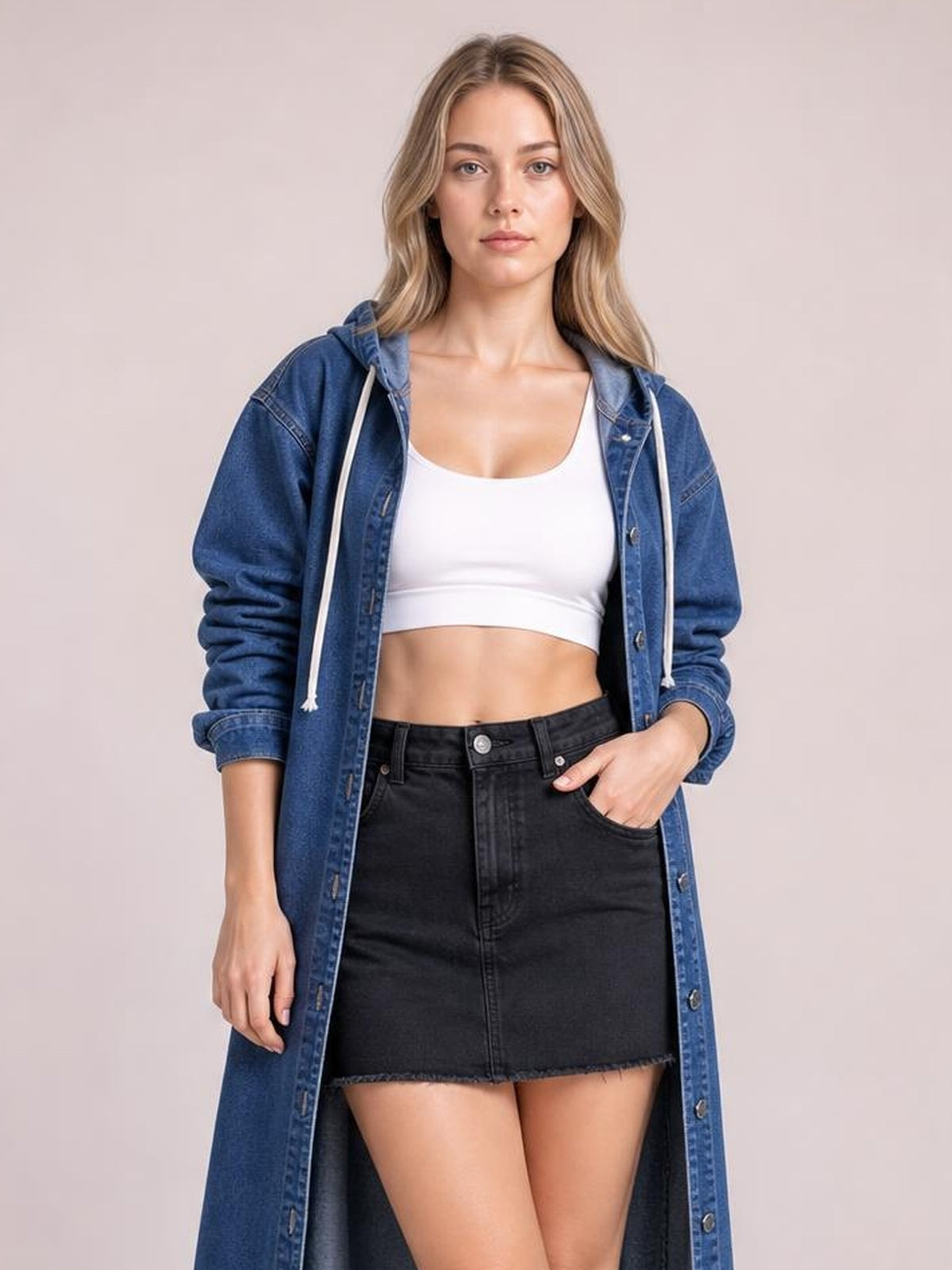 A model wears a blue longline denim shirt with a hood, button front, and long sleeves, styled open in a relaxed silhouette with one hand in her pocket.
