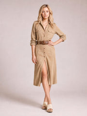Model poses in a tan button-up long sleeve shirt dress with chest pockets, a belted waist, and a straight midi silhouette with front slit.