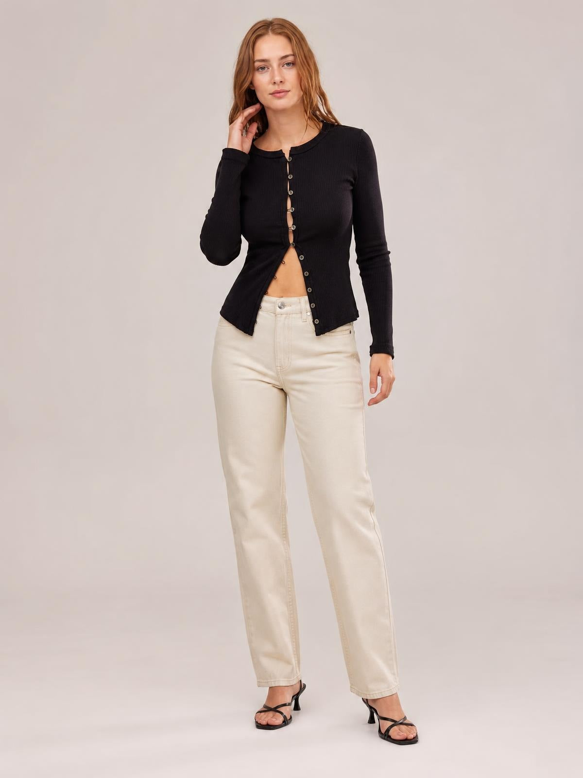 A model poses in a fitted black ribbed cardigan with a round neck, long sleeves, and button-front construction, worn partially open at the waist.