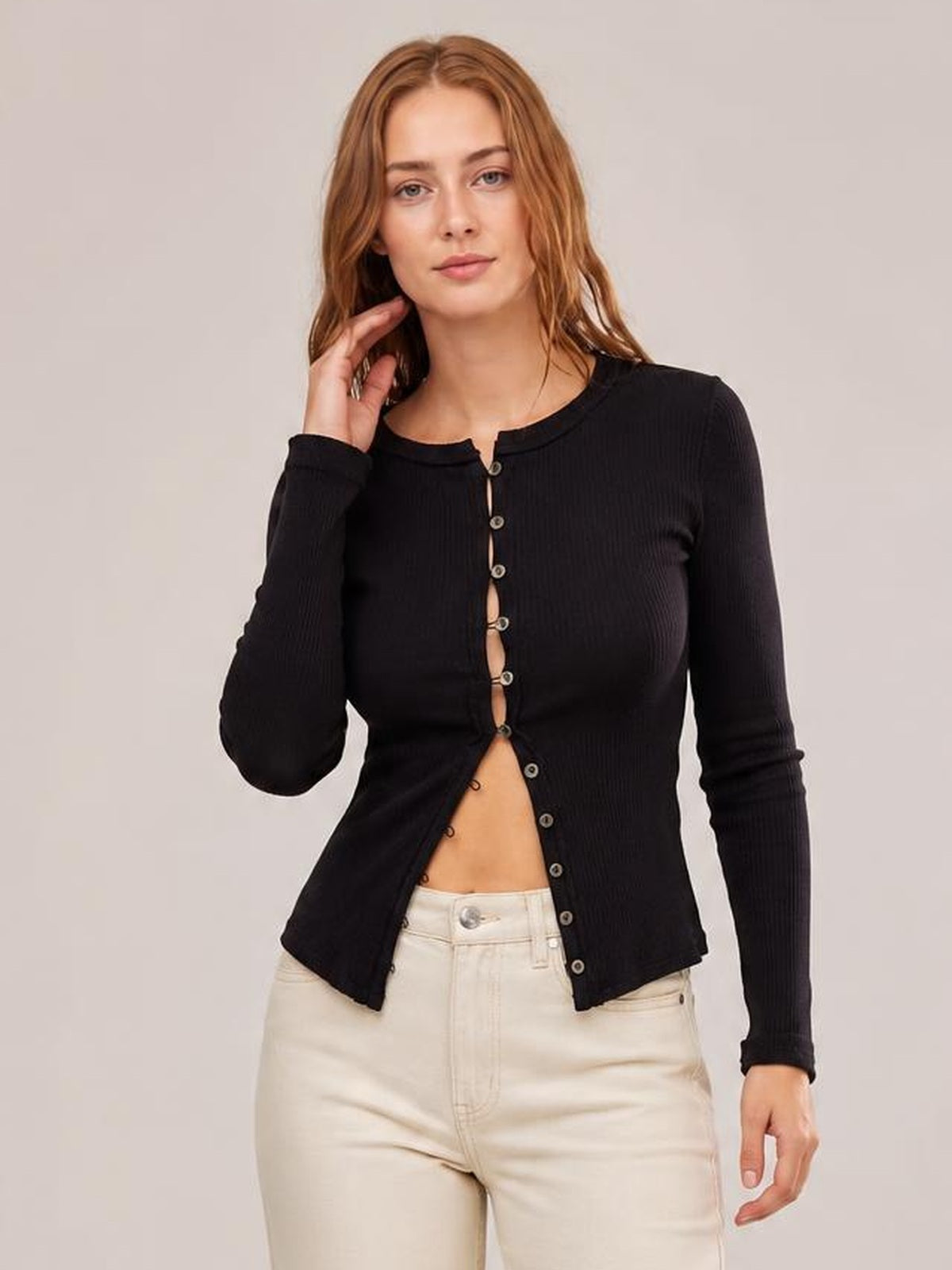 A model poses in a fitted black ribbed cardigan with a round neck, long sleeves, and button-front closure worn partially open.