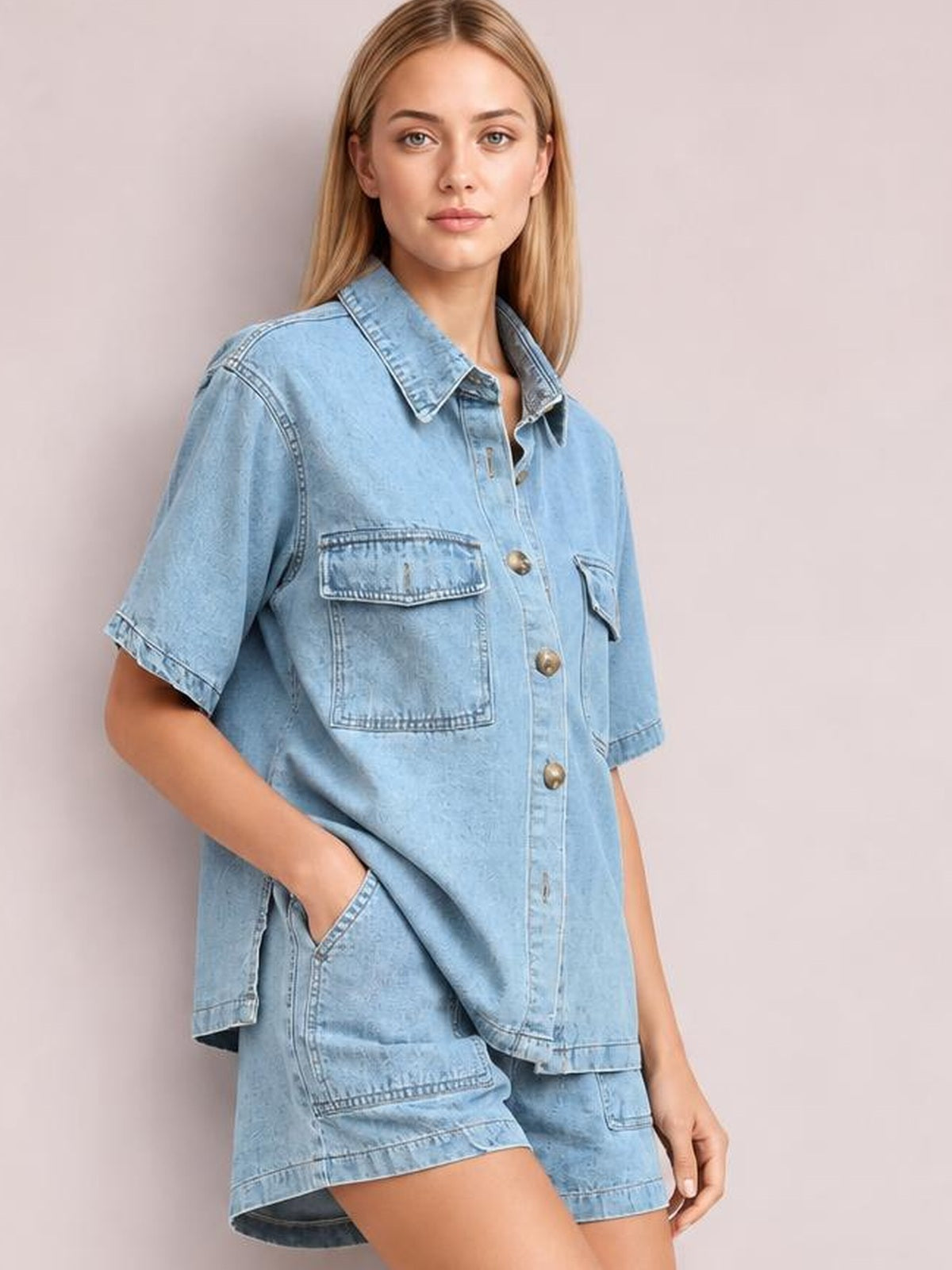 A model poses with one hand in her pocket wearing a light blue denim button-up short sleeve top and matching pocketed shorts in a relaxed silhouette.