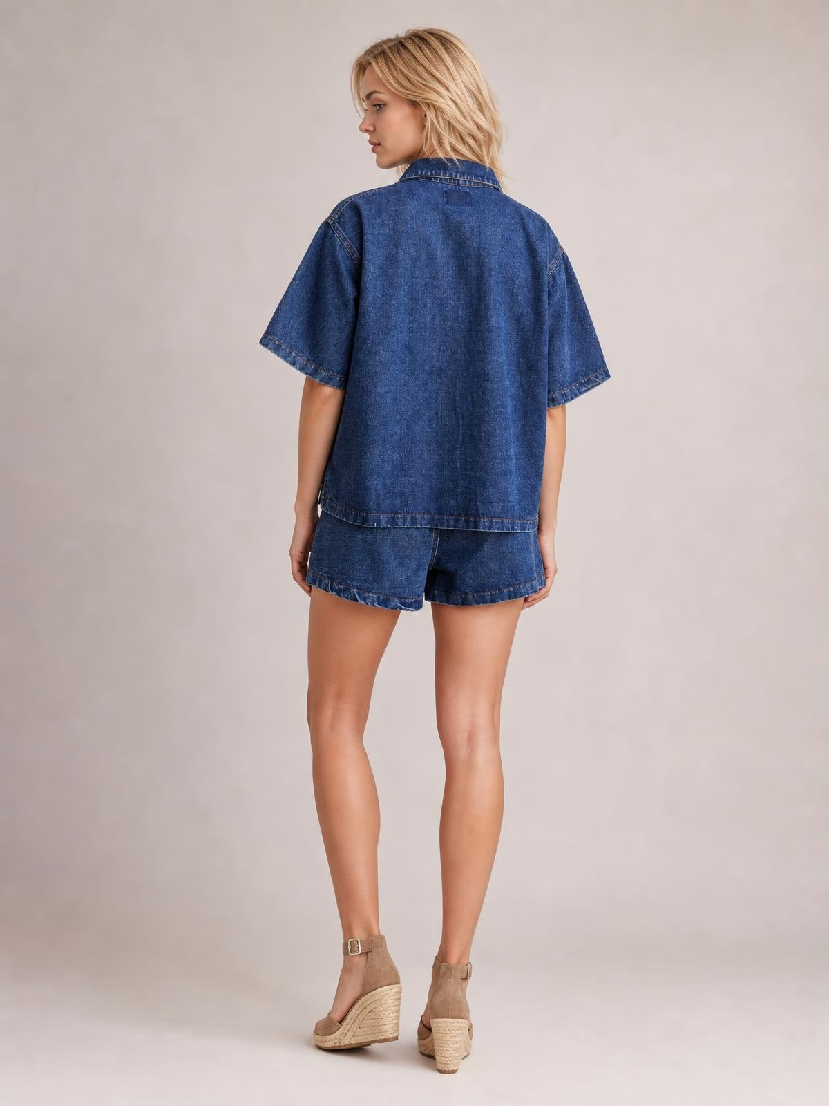 Model shown from the back in a blue denim set with a loose button-up short-sleeve top, pointed collar, and matching pocketed shorts.