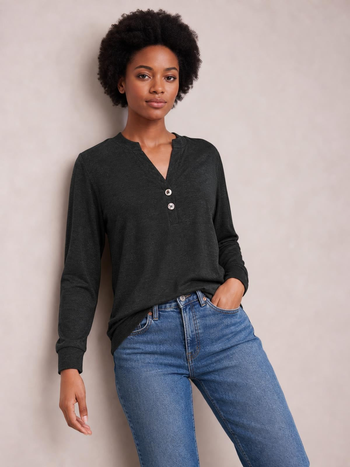 Model wearing a charcoal long-sleeve top with a notched neck, two-button placket, relaxed silhouette, and ribbed cuffs, posing with one hand in her jeans pocket.