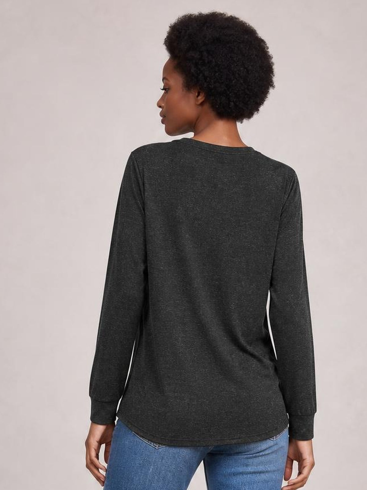 A model is shown from the back wearing a dark charcoal long-sleeve top with a relaxed straight silhouette, fitted cuffs, and a gently curved hem.