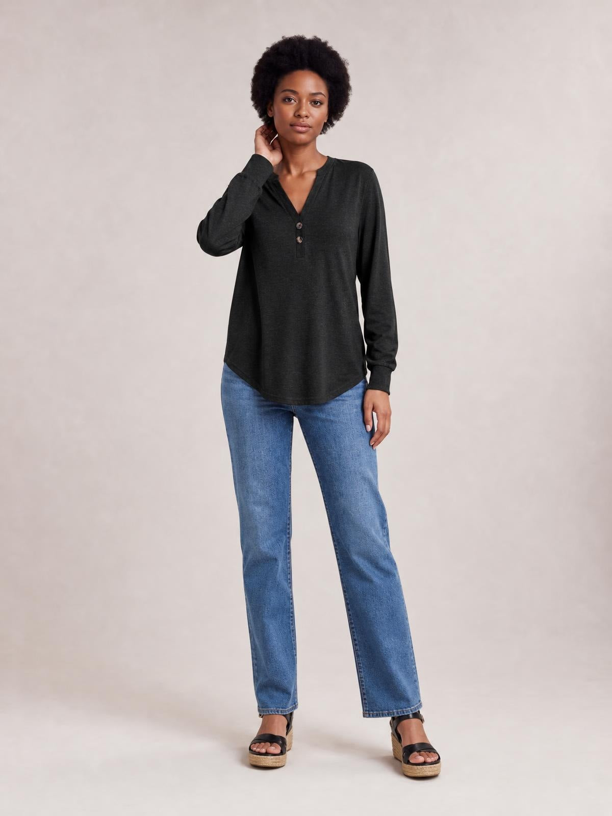 Model wears a charcoal buttoned notched-neck long-sleeve top with a relaxed silhouette, front button placket, and curved hem while standing in jeans.