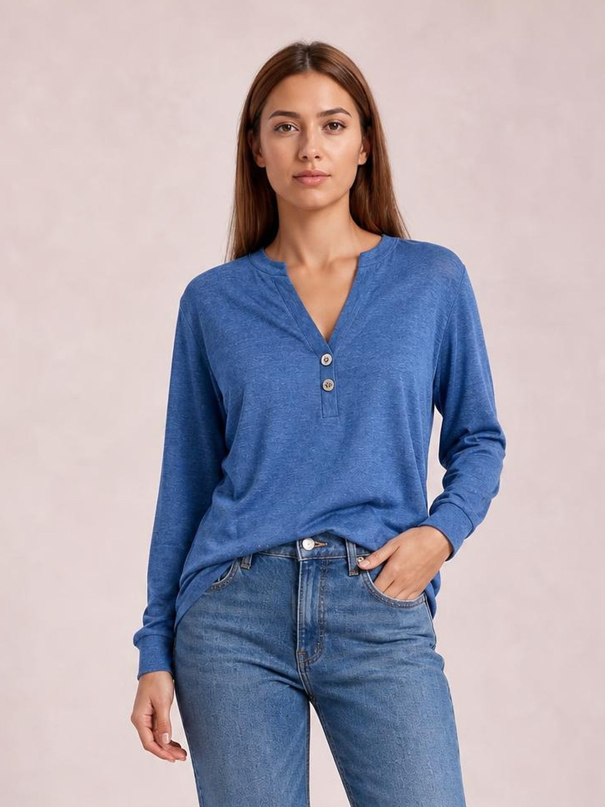 Model wearing a blue long sleeve top with a notched neck, buttoned placket, subtle texture, and relaxed silhouette, posing with one hand in her jeans pocket.
