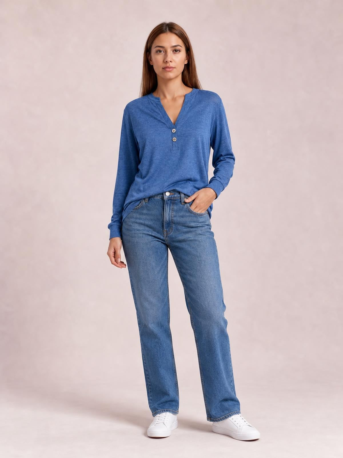 A model stands in a blue buttoned notched-neck long-sleeve top with a relaxed silhouette, V-shaped opening, and straight hem styled with jeans.